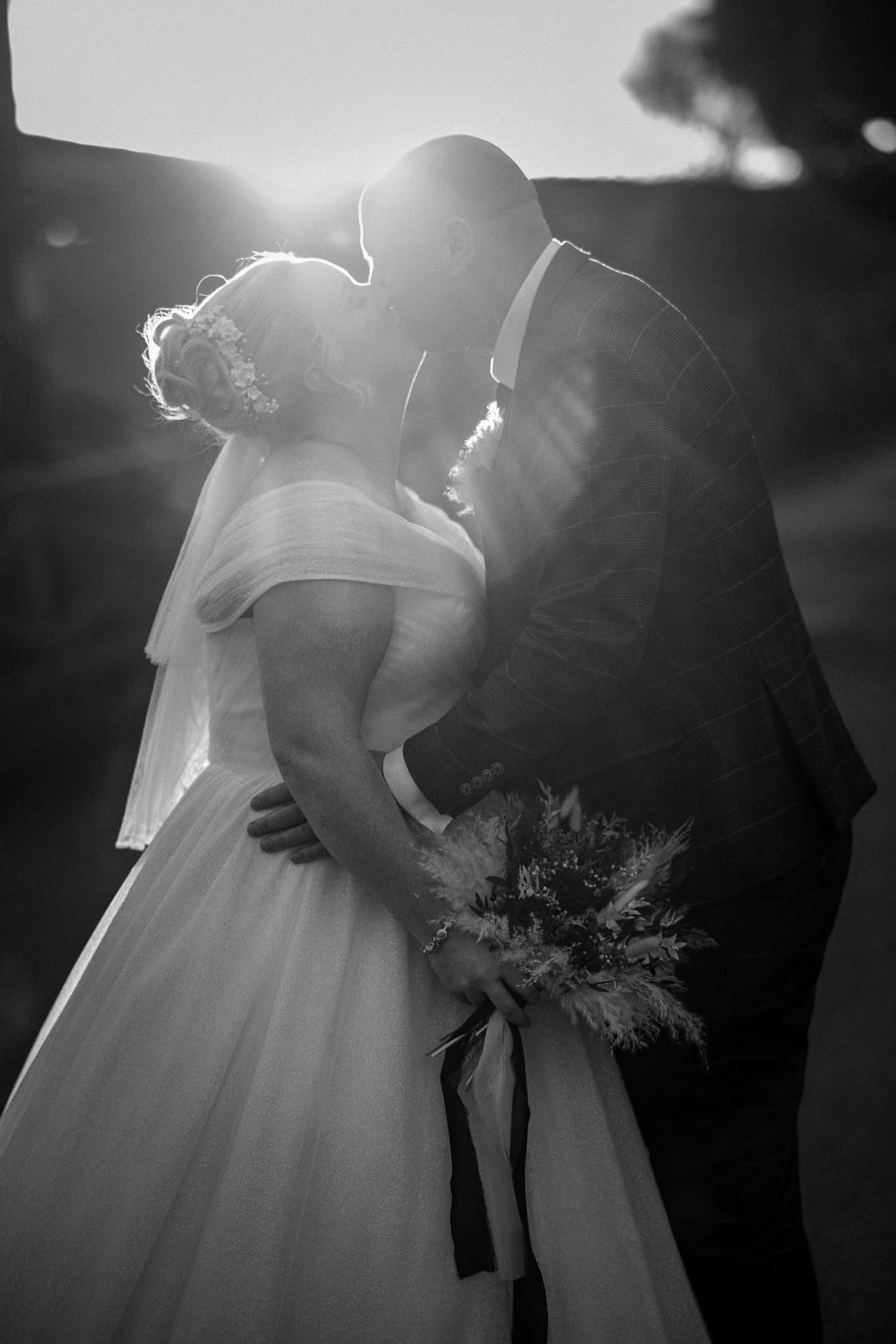 Ethereal black and white wedding photos show a bride in flowing dress backlit by sunlight creating a dreamy silhouette.