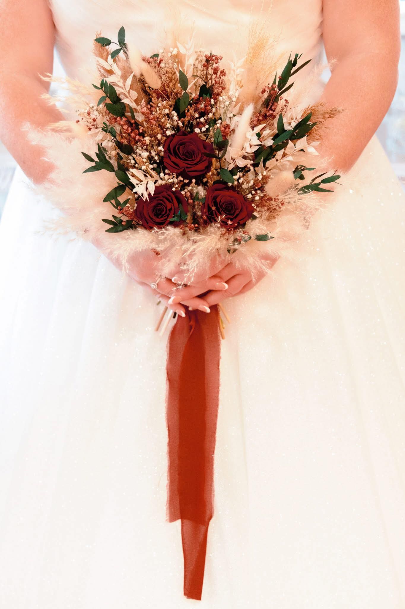 Close-up of pink and burgundy wedding bouquets with roses and greenery wrapped in ribbon.