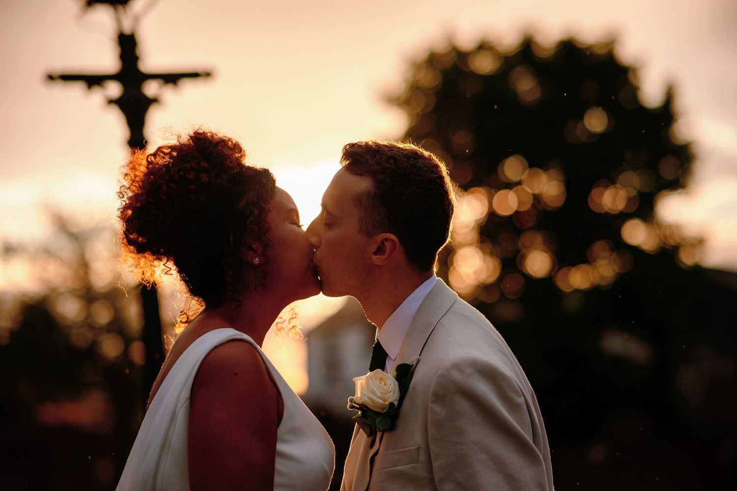 A silhouetted couple shares a romantic moment at sunset with warm golden light in the background.