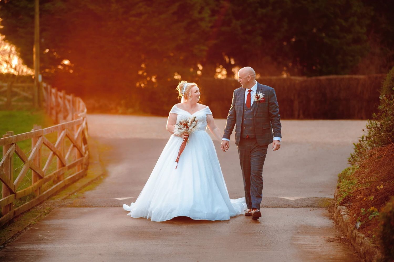 A couple walking together on an illuminated pathway at dusk, with the bride in a white gown and groom in dark suit.