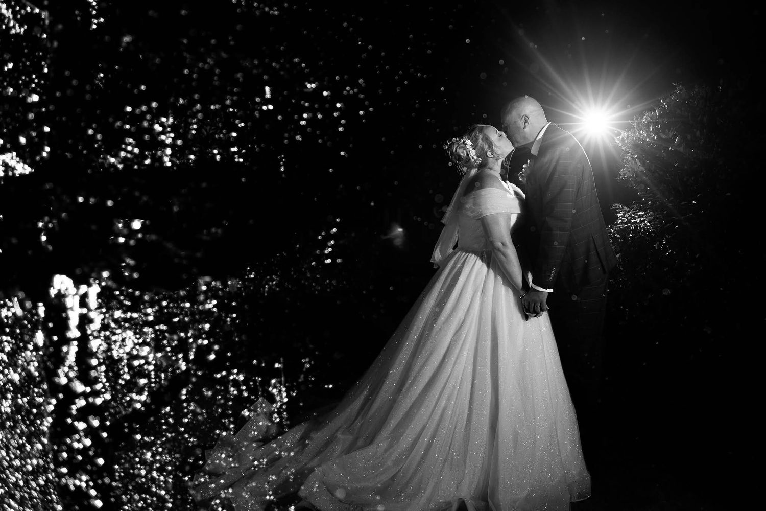 Dramatic black and white silhouettes of a bride and groom dancing with lens flare effects.