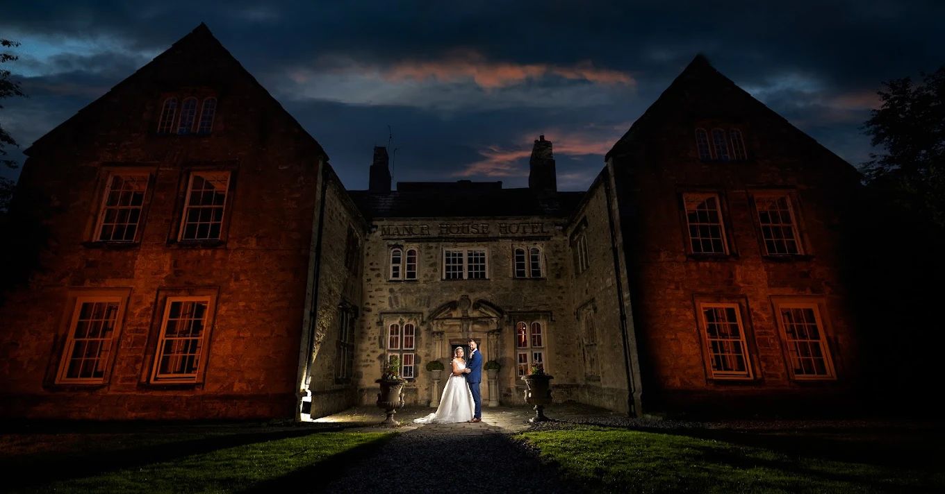 A historic stone building illuminated at dusk with dramatic cloudy skies overhead.