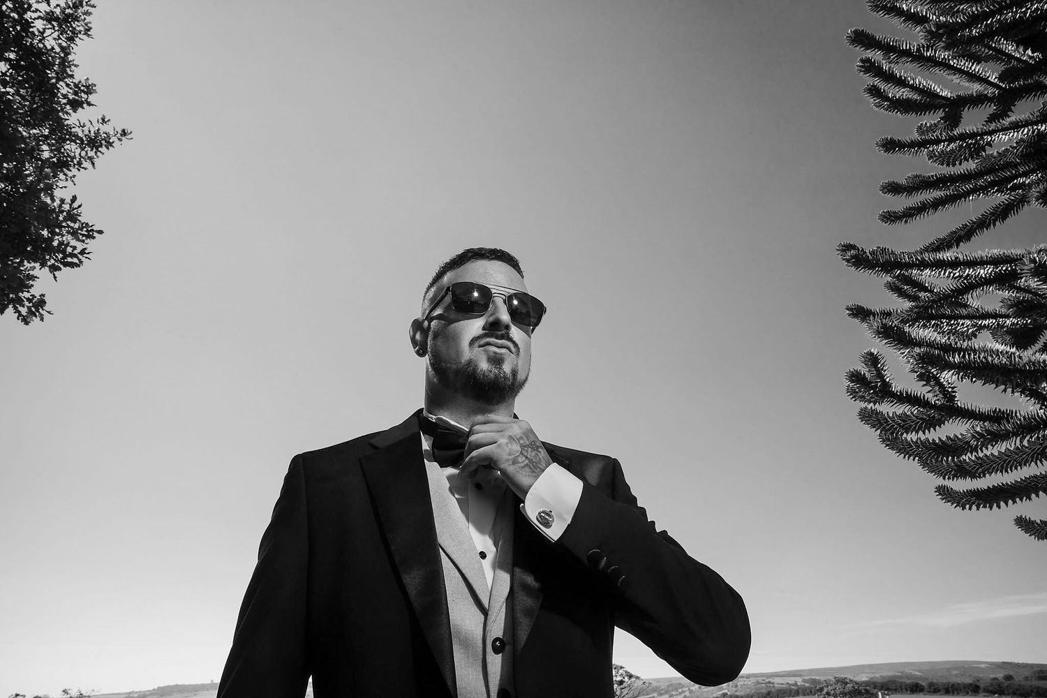 Black and white portrait of groomsmen in formal attire against sky background.