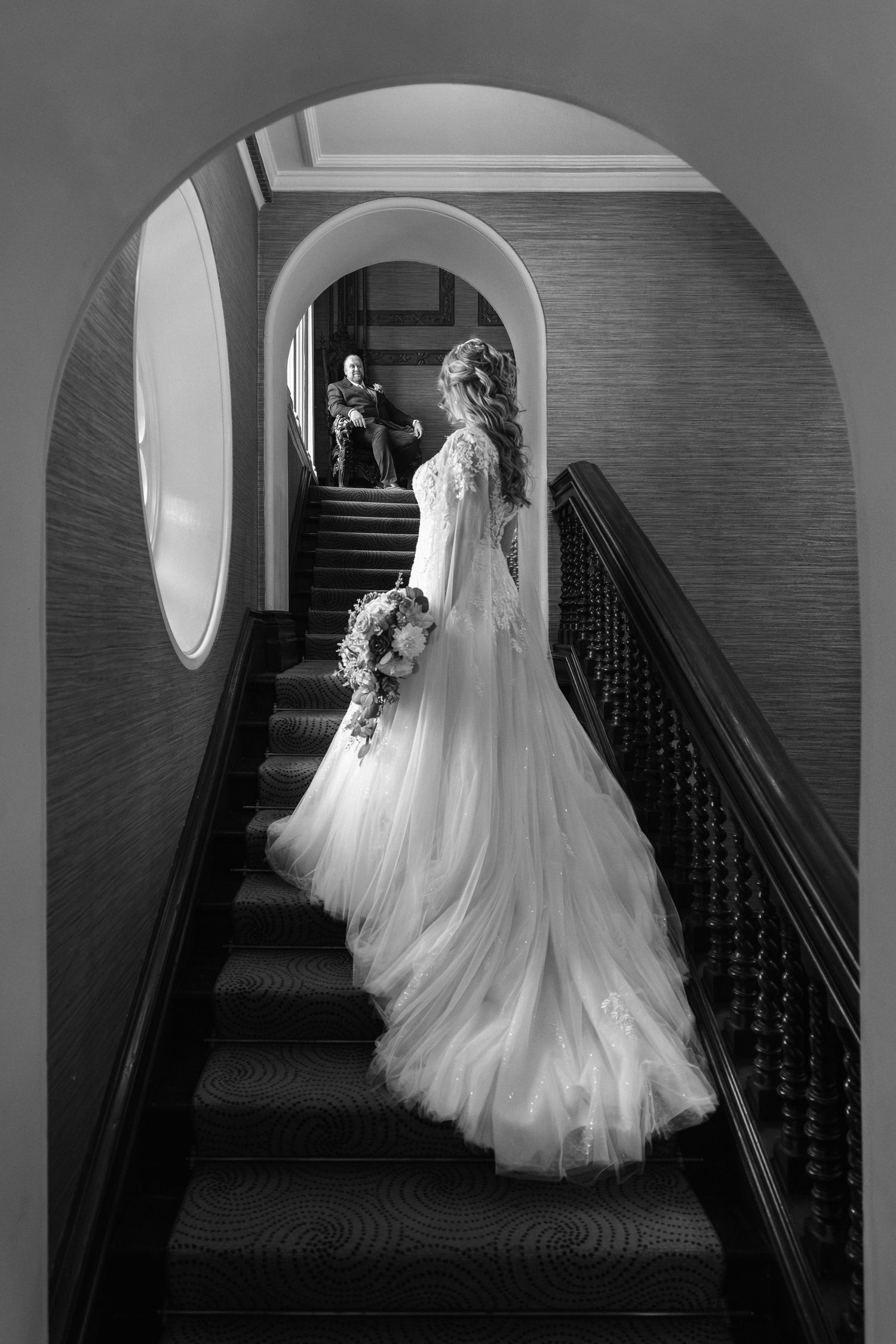 A black and white photo series showing a bride in a flowing wedding gown descending a grand staircase.