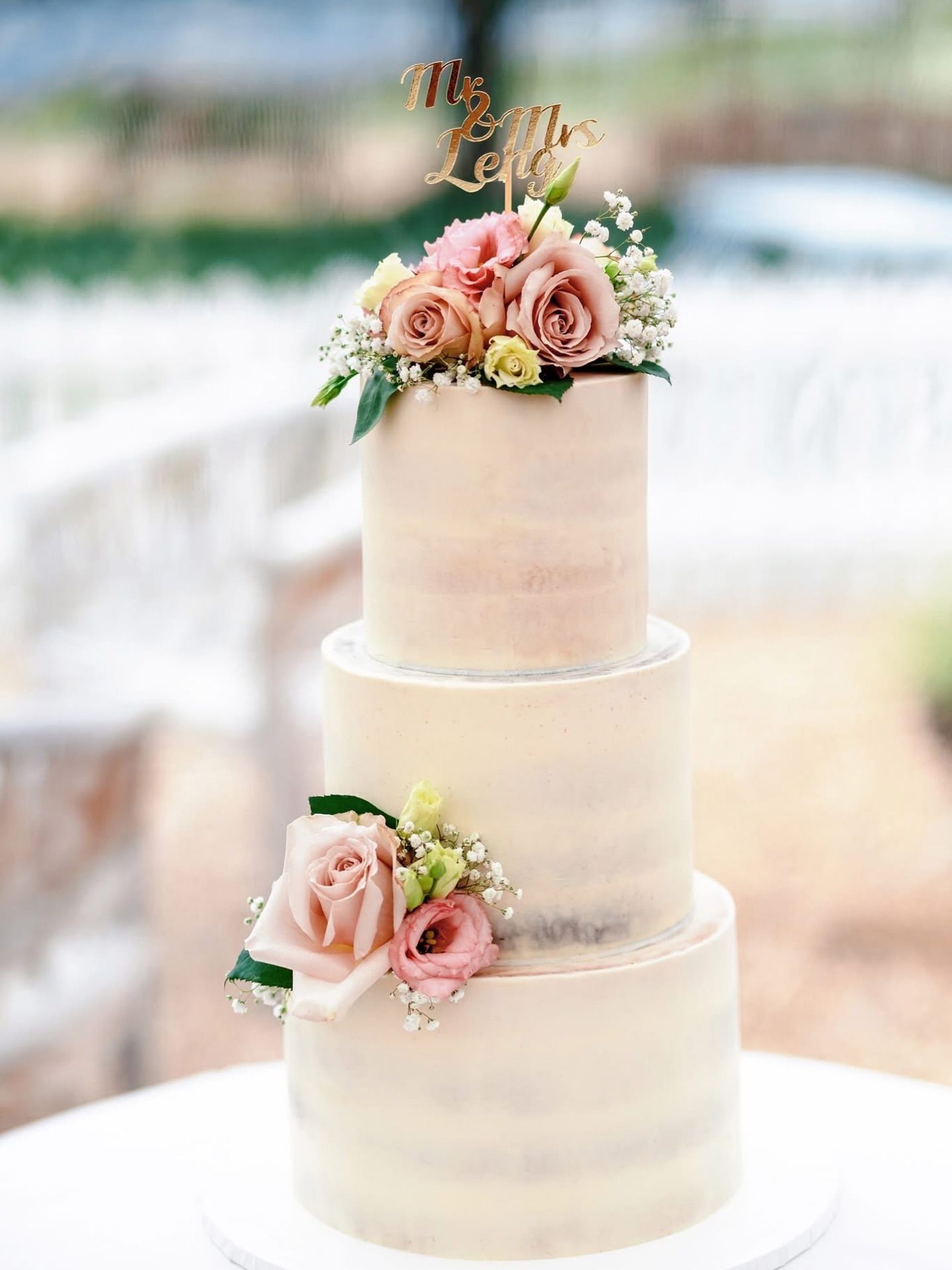 Elegant white wedding cake decorated with fresh pink roses and greenery.