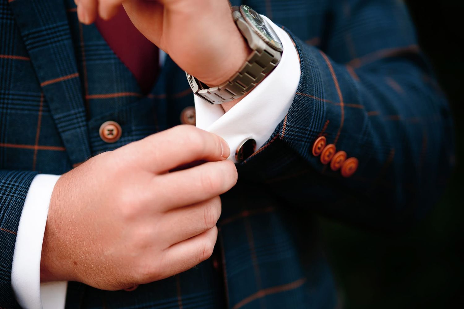 Close-up of hands adjusting a white dress shirt cuff with a plaid suit jacket sleeve.