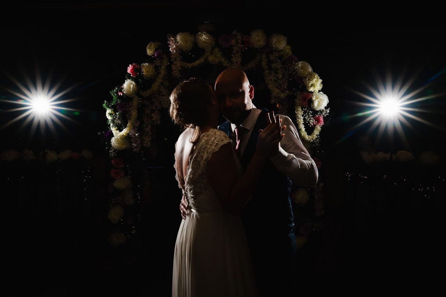 Wedding couple shares their first dance together under twinkling lights at an evening reception celebration.