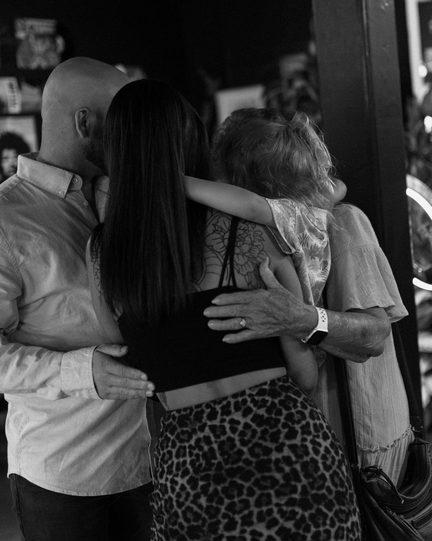 Black and white photo of a family embracing from behind, showing a man, woman, and child hugging.