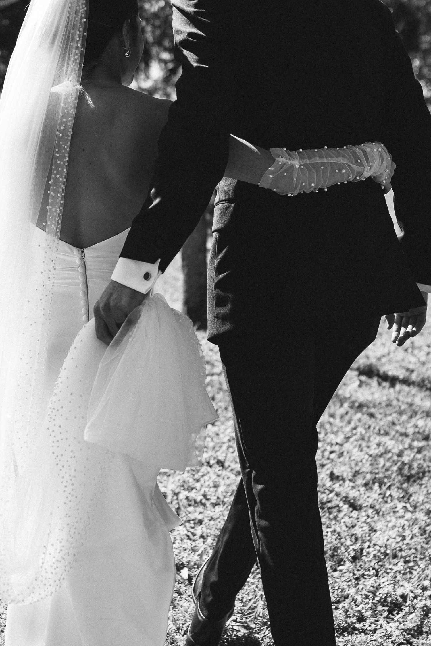 Black and white photo of bride and groom walking hand in hand outdoors on wedding day.