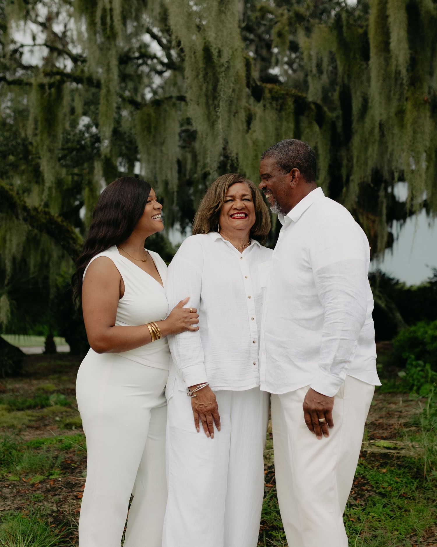 Three-generation family portrait with woman and two adults laughing in white outfits outdoors.