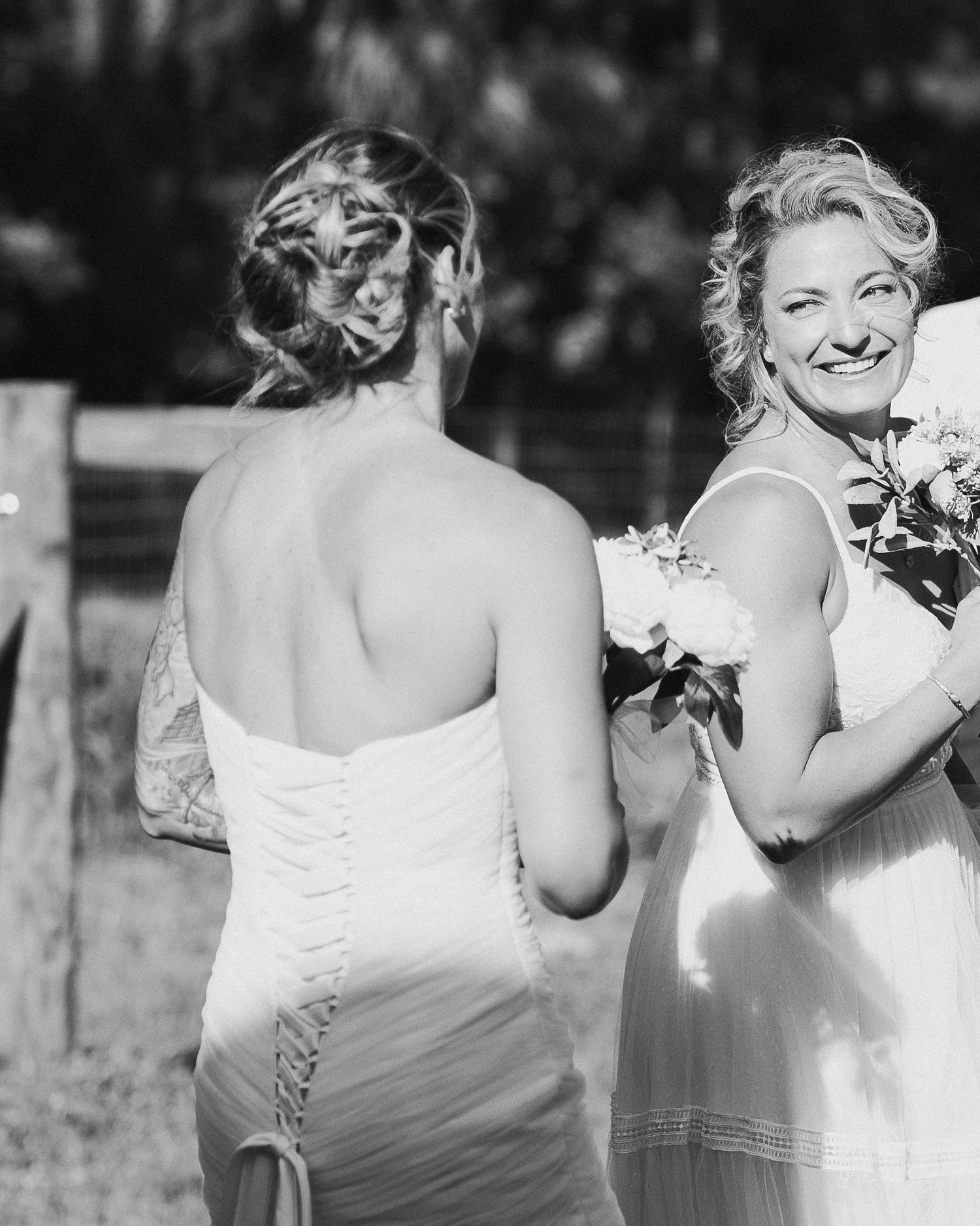 Black and white photo of two brides sharing a joyful moment during their outdoor wedding ceremony.