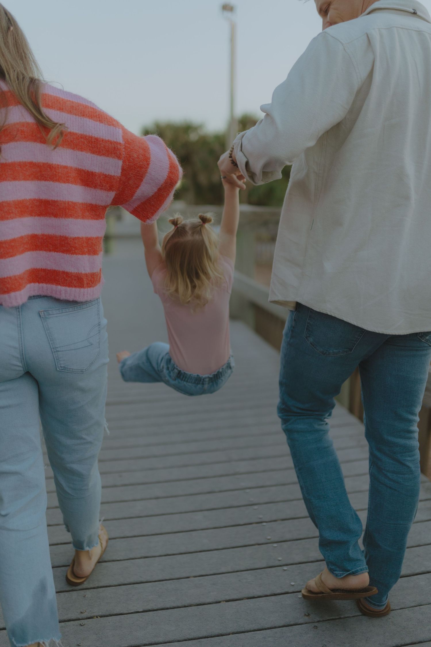 A family of three walks on a wooden boardwalk, parents swinging their young daughter between them.