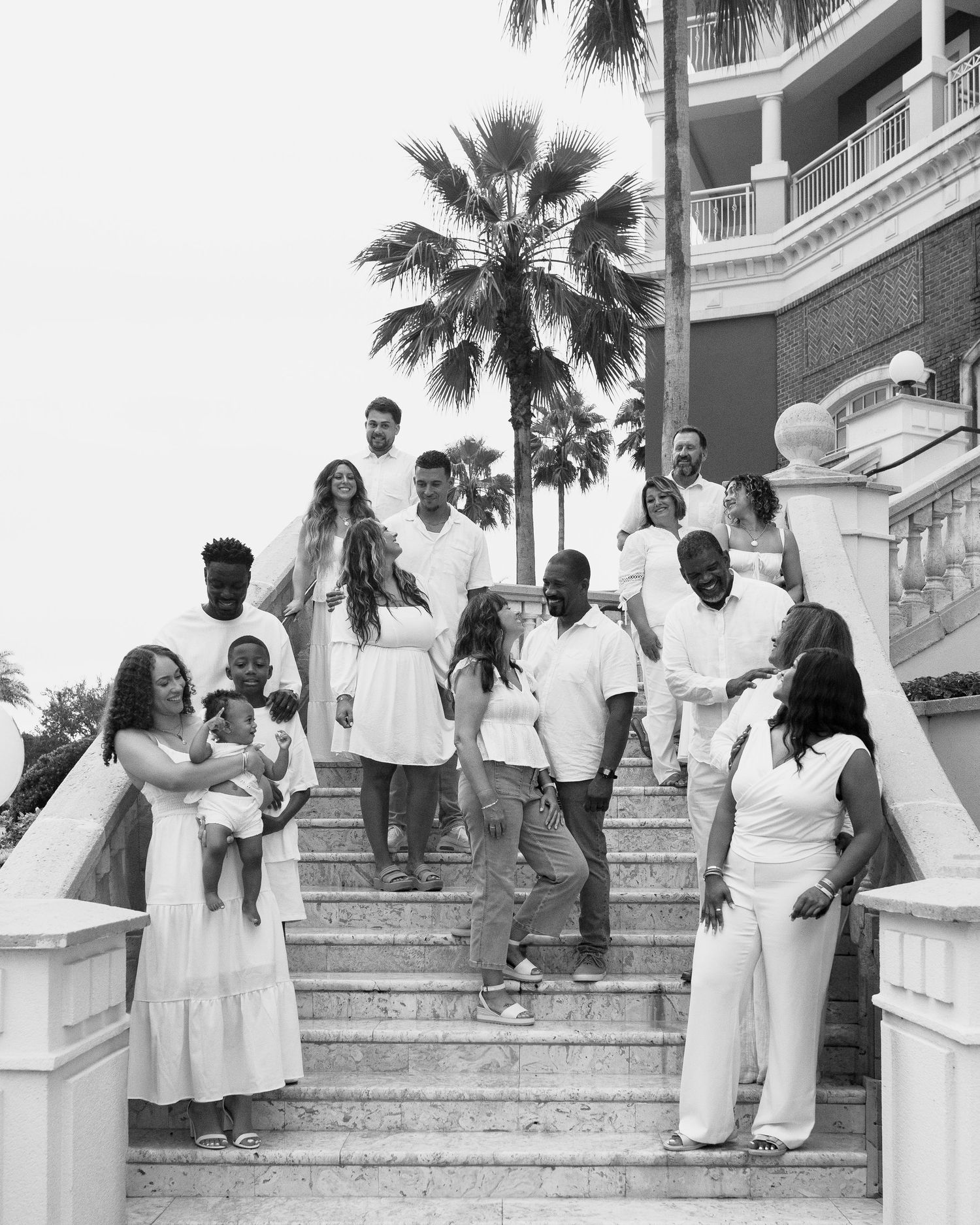 Black and white photo of extended family in white outfits descending outdoor staircase with palms.