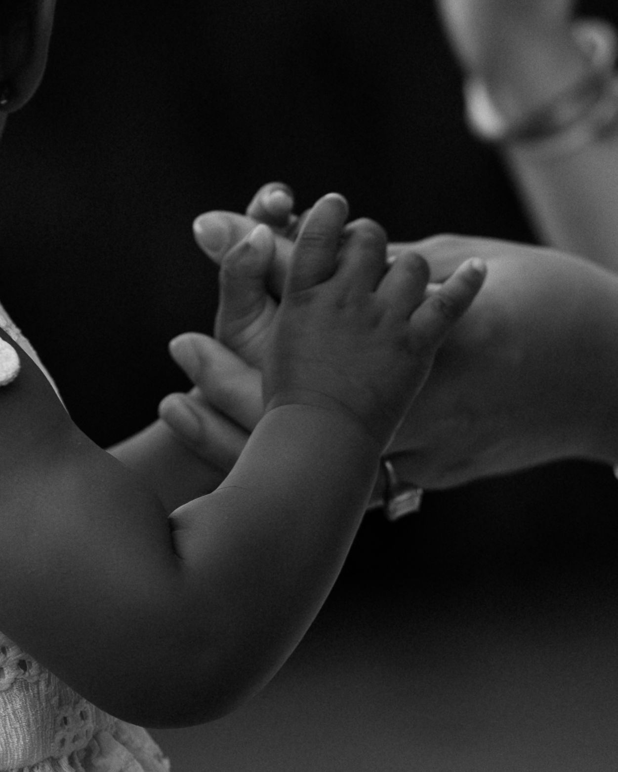 Black and white macro photo of an adult tenderly holding a baby's tiny hands.