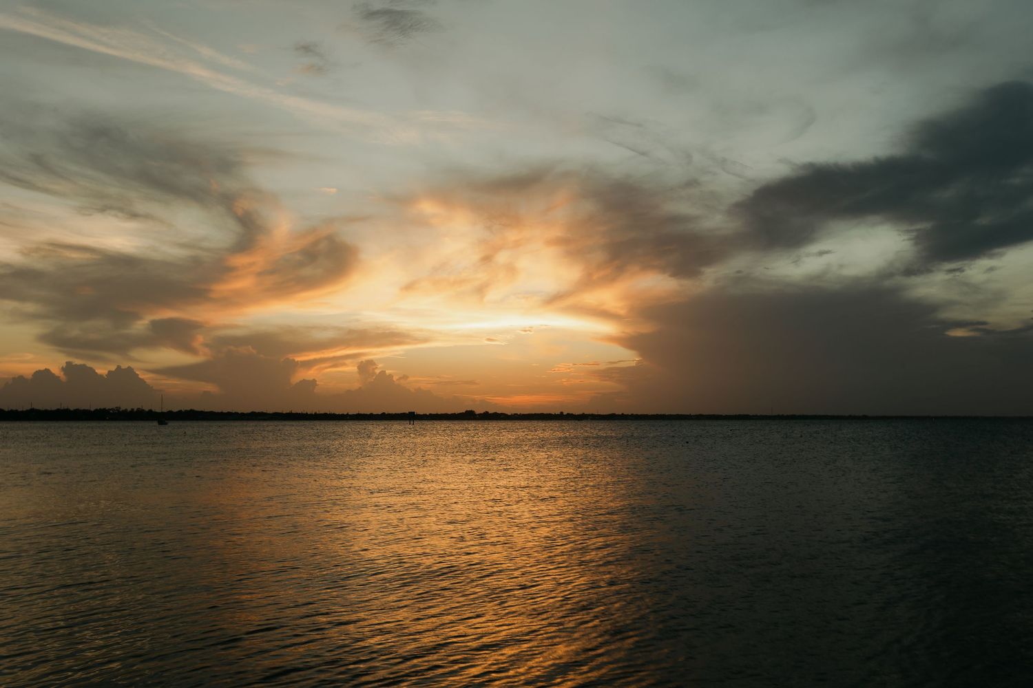 Dramatic golden sunset over calm water with dark storm clouds illuminated by warm orange light.