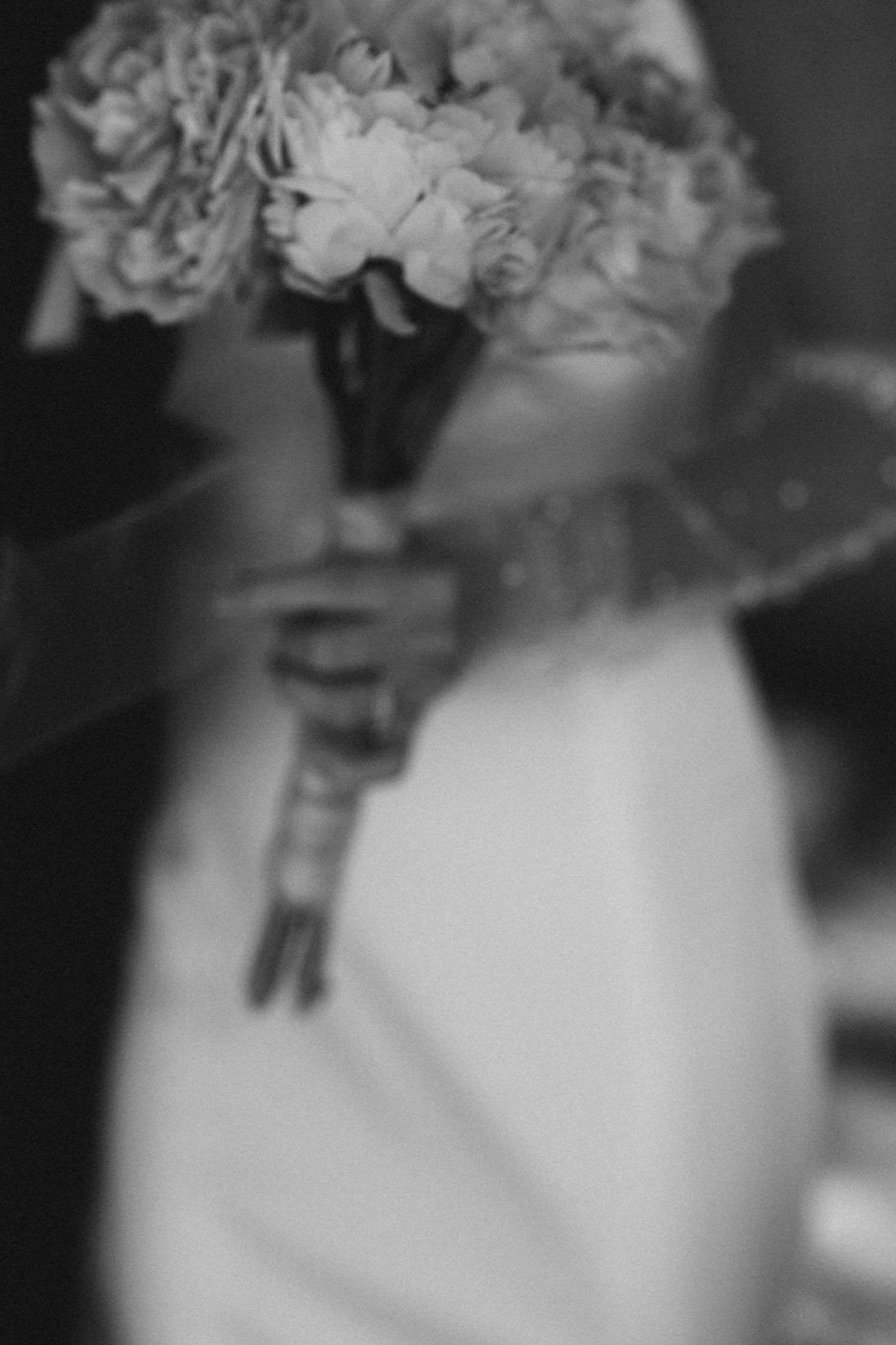 Close-up black and white photo of bride holding elegant floral bouquet on wedding day.