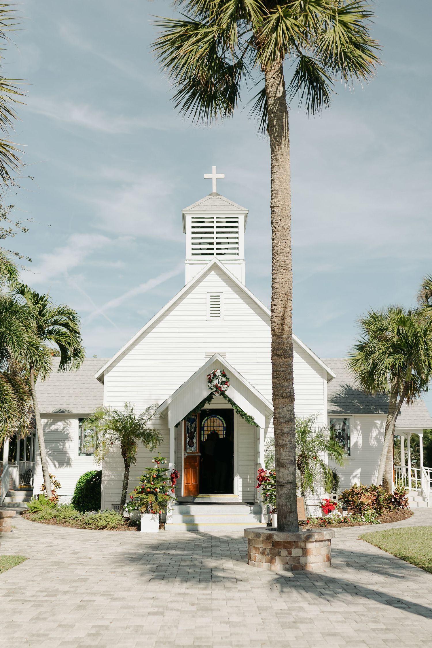 A charming white wooden chapel with a cross steeple surrounded by palm trees in Florida.