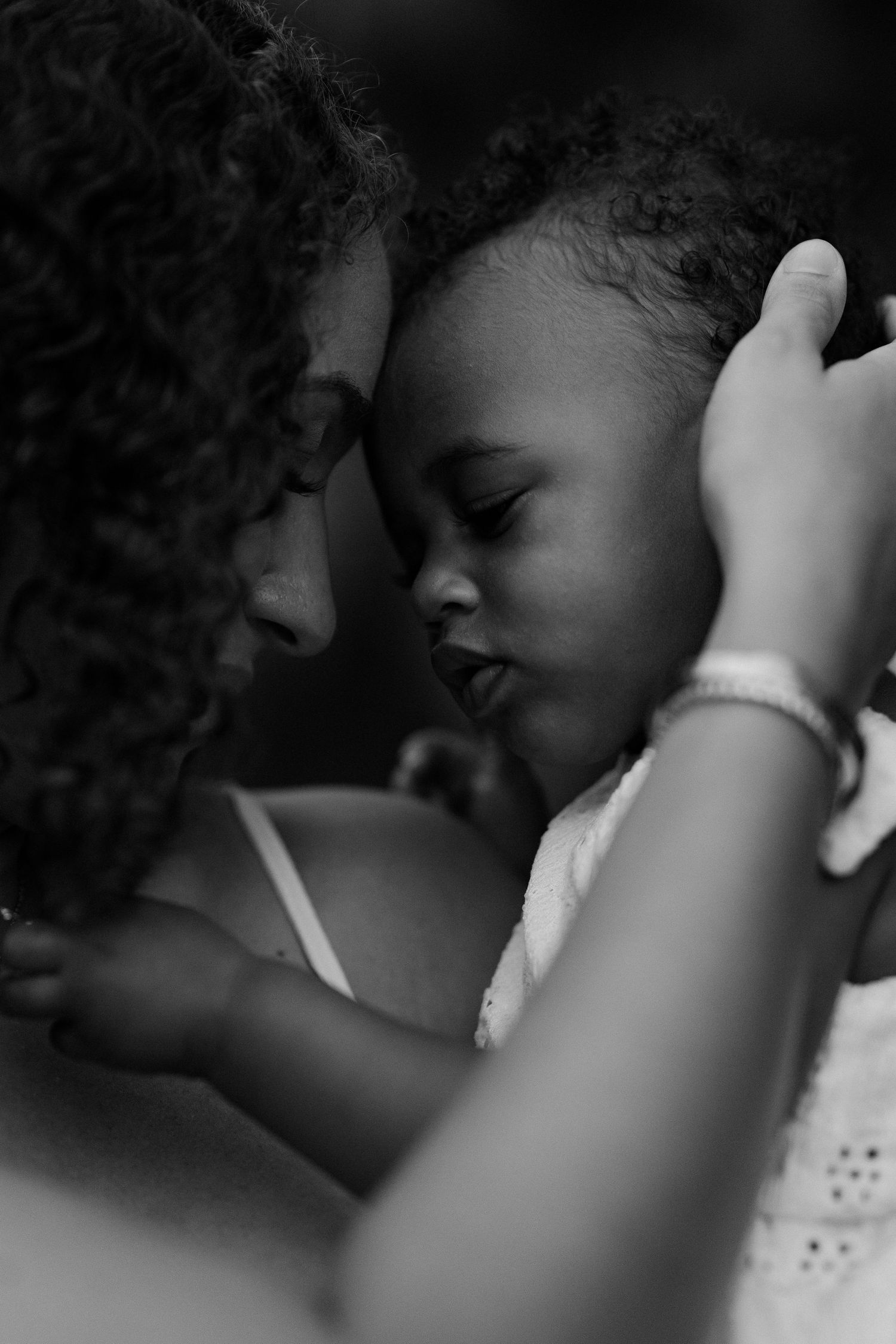 Intimate black and white close-up of a mother gently touching foreheads with her sleeping baby.