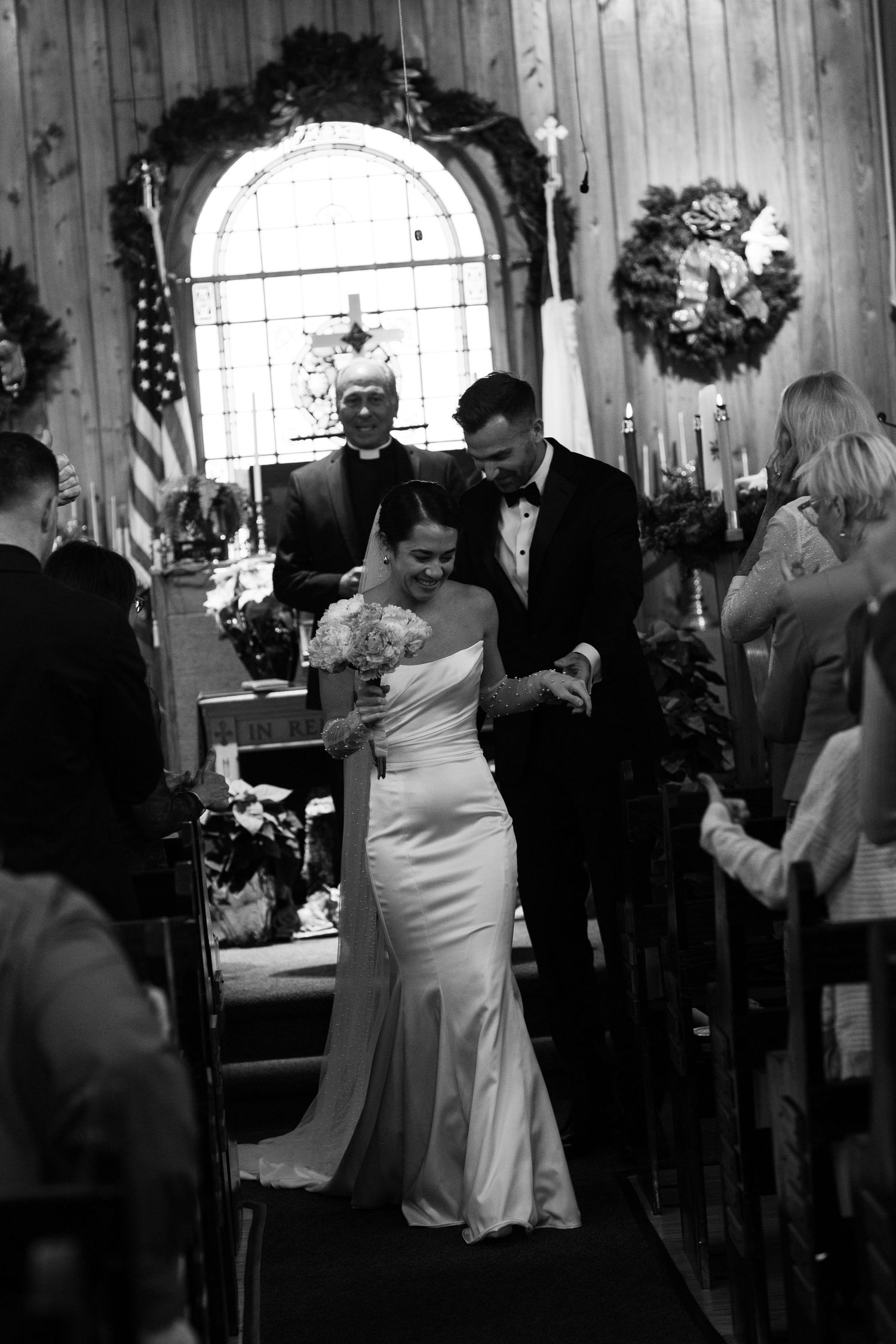 Black and white photo of a bride and groom walking down the aisle after their church ceremony.
