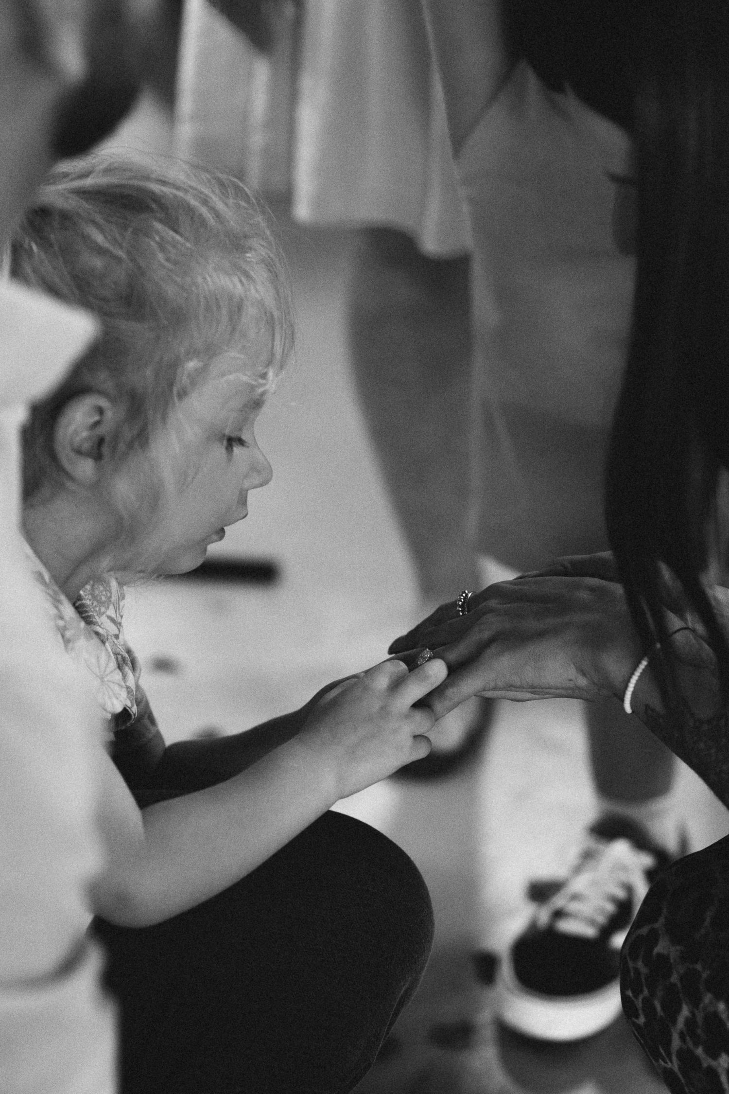 A young blonde child examines an adult's hand in a tender black and white moment.