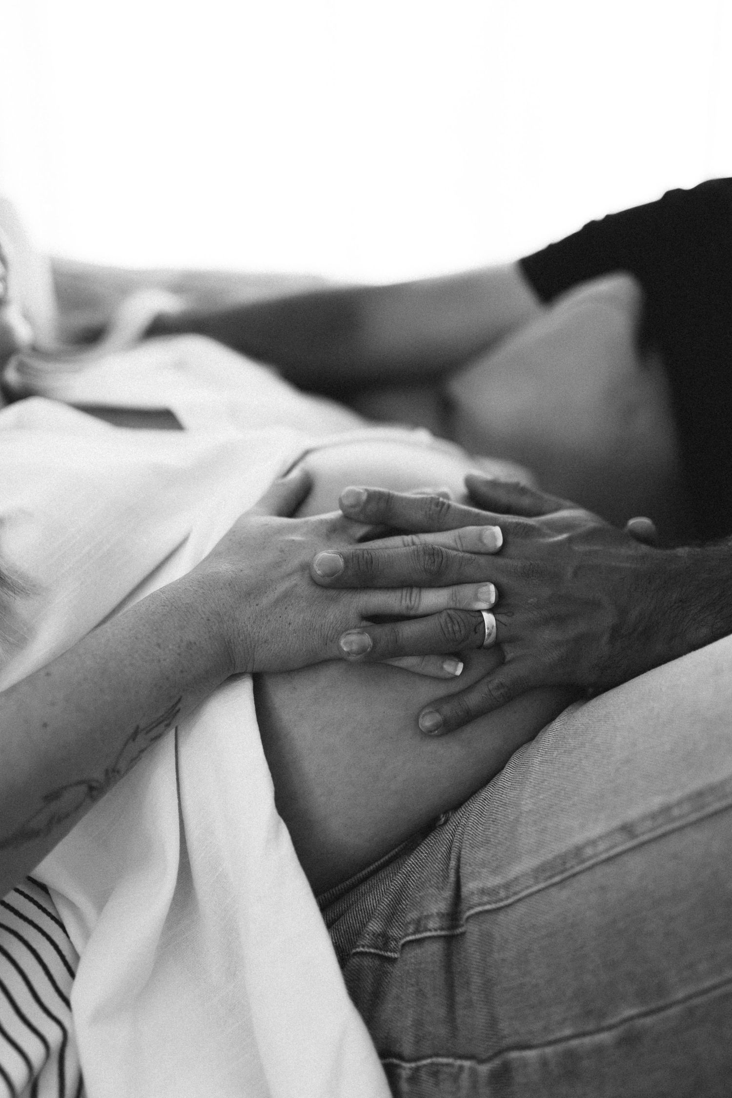 Black and white photo of couple's hands tenderly resting on pregnant belly, capturing a intimate maternity moment.