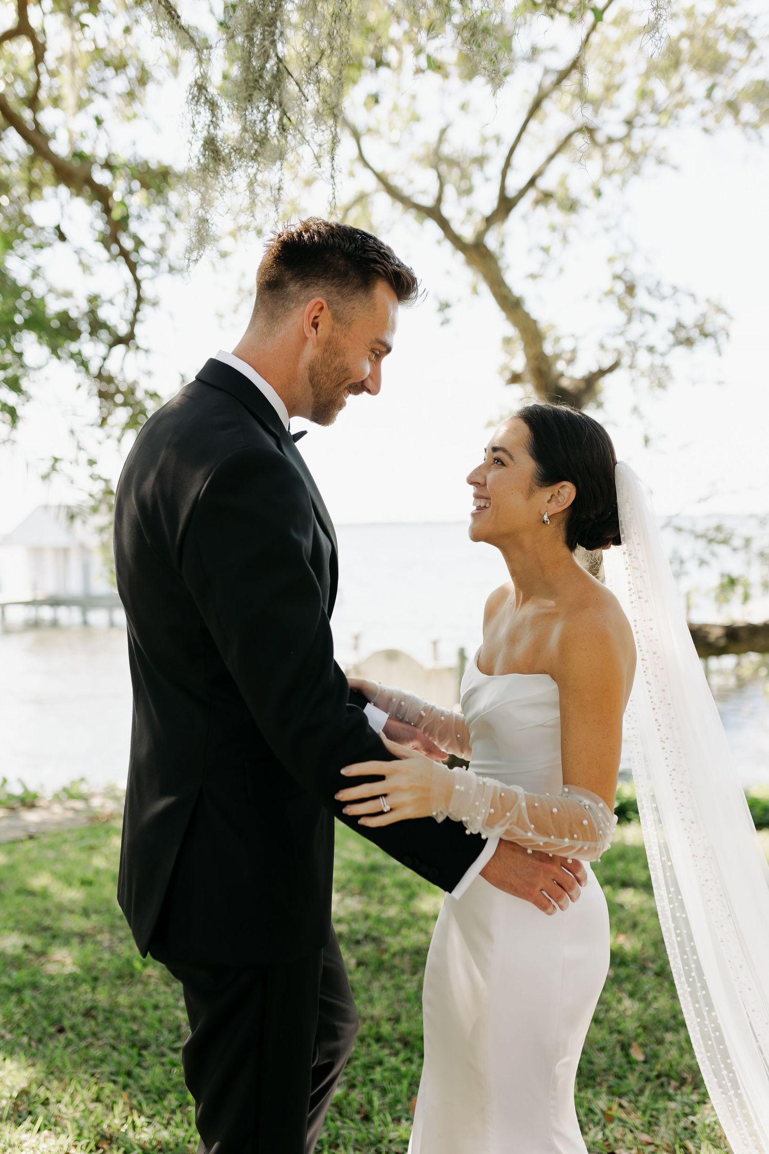 Bride and groom gazing at each other lovingly near waterfront in outdoor wedding portrait.