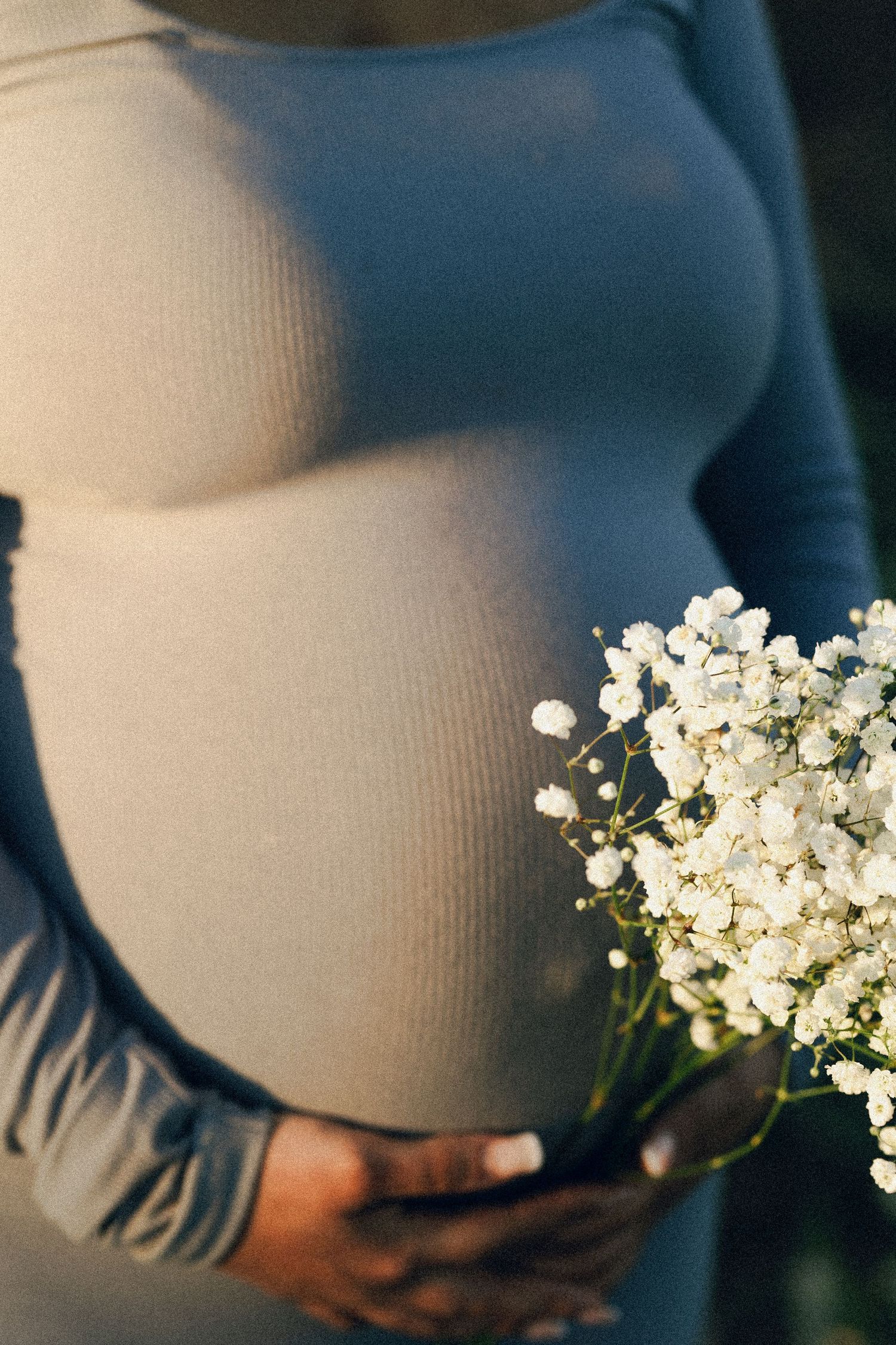 Close-up of pregnant woman in blue dress holding white baby's breath flowers.