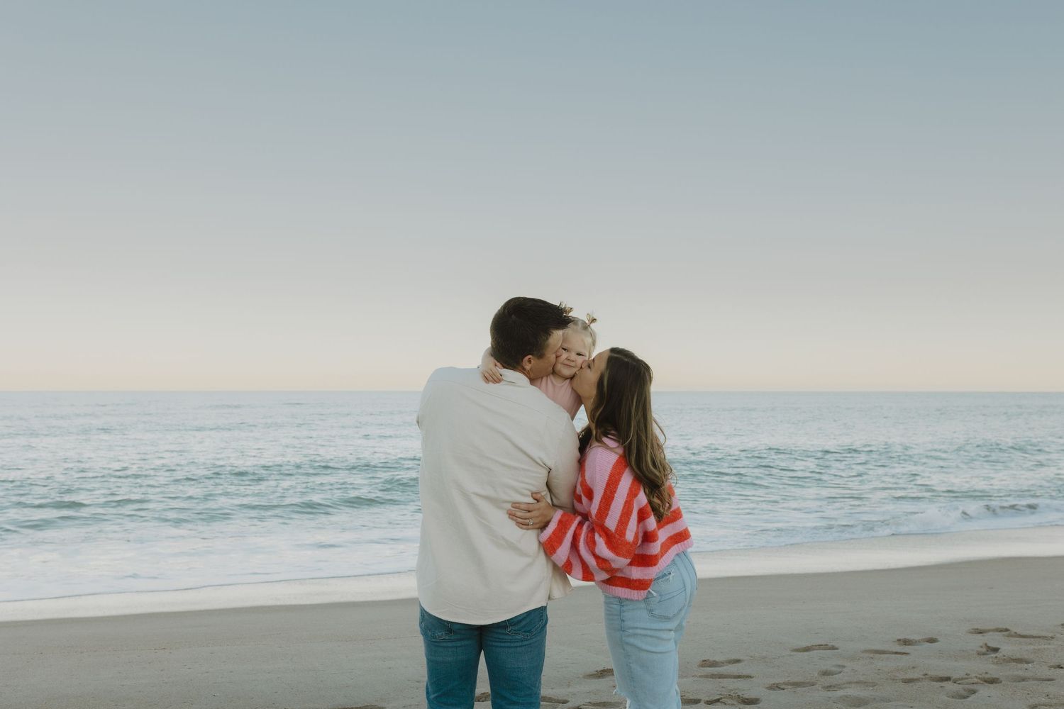 Couple sharing a kiss on the beach at sunset with gentle ocean waves behind them.