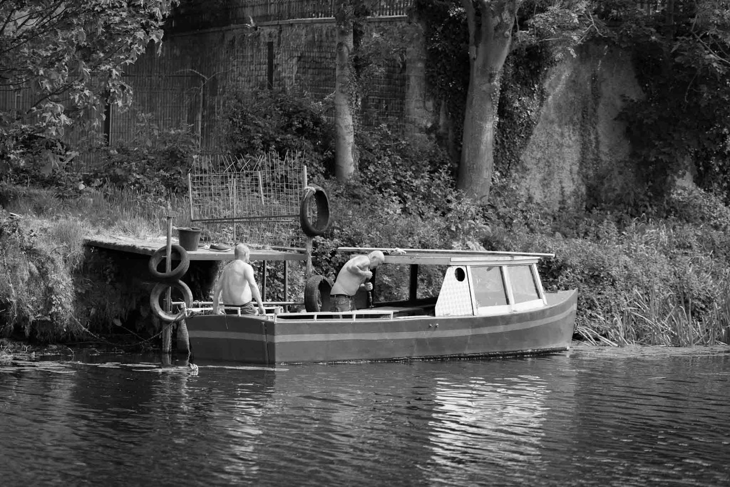 A male sitting at the end of a small boat, relaxing with his shirt off in the summer.