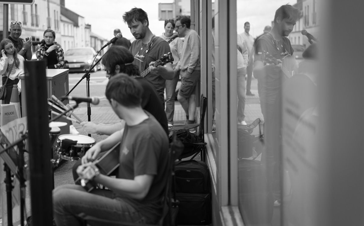 Mono image of buskers outside a shop.