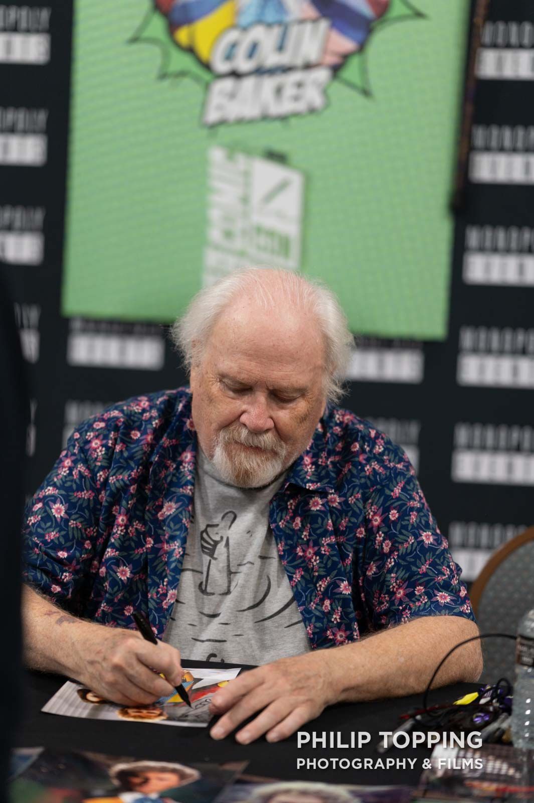 Colin Baker is looking down at the signing.