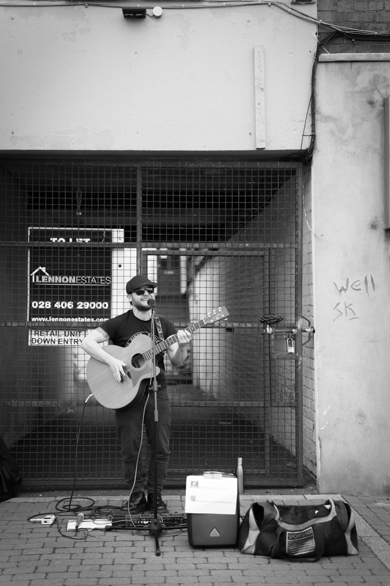 A singer playing guitar in front of a tall fence.