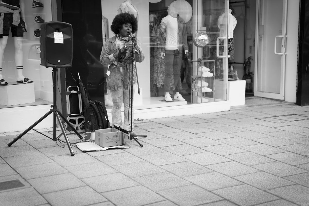Dark skinned singer performing in front of a shop with a speaker beside her.