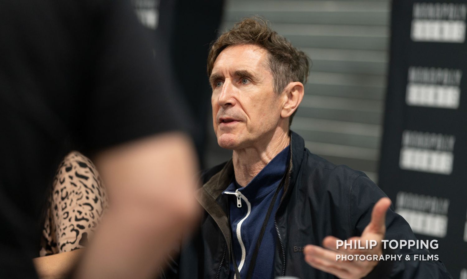Paul McGann from the Doctor Who TV movie is talking to someone with a hand raised.