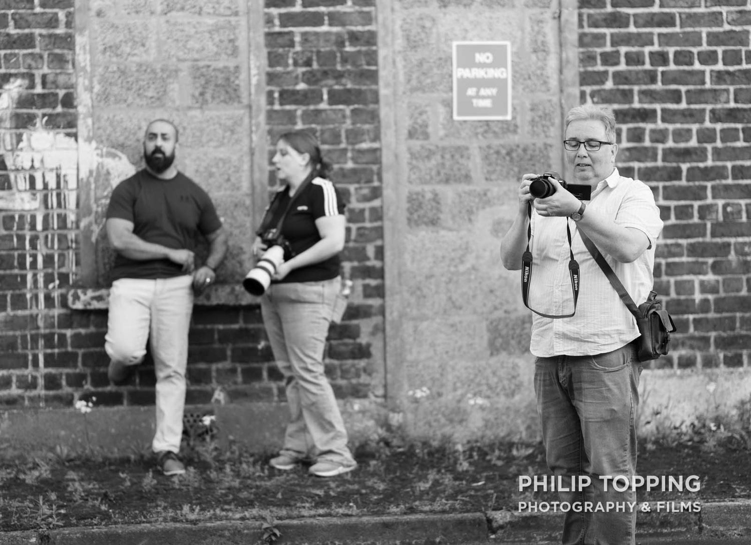 Member of Focus Photography Club taking a photo in front of a brick wall.