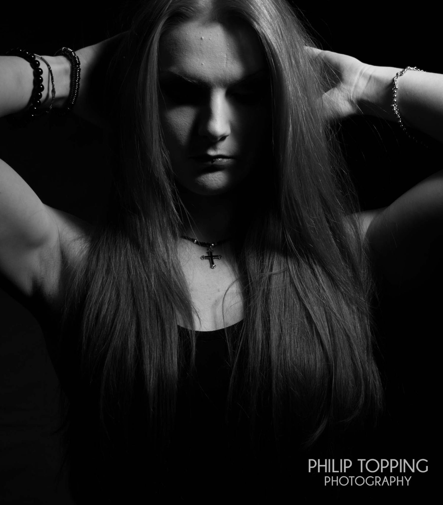 Moody mono image of a female with her hands behind her head.