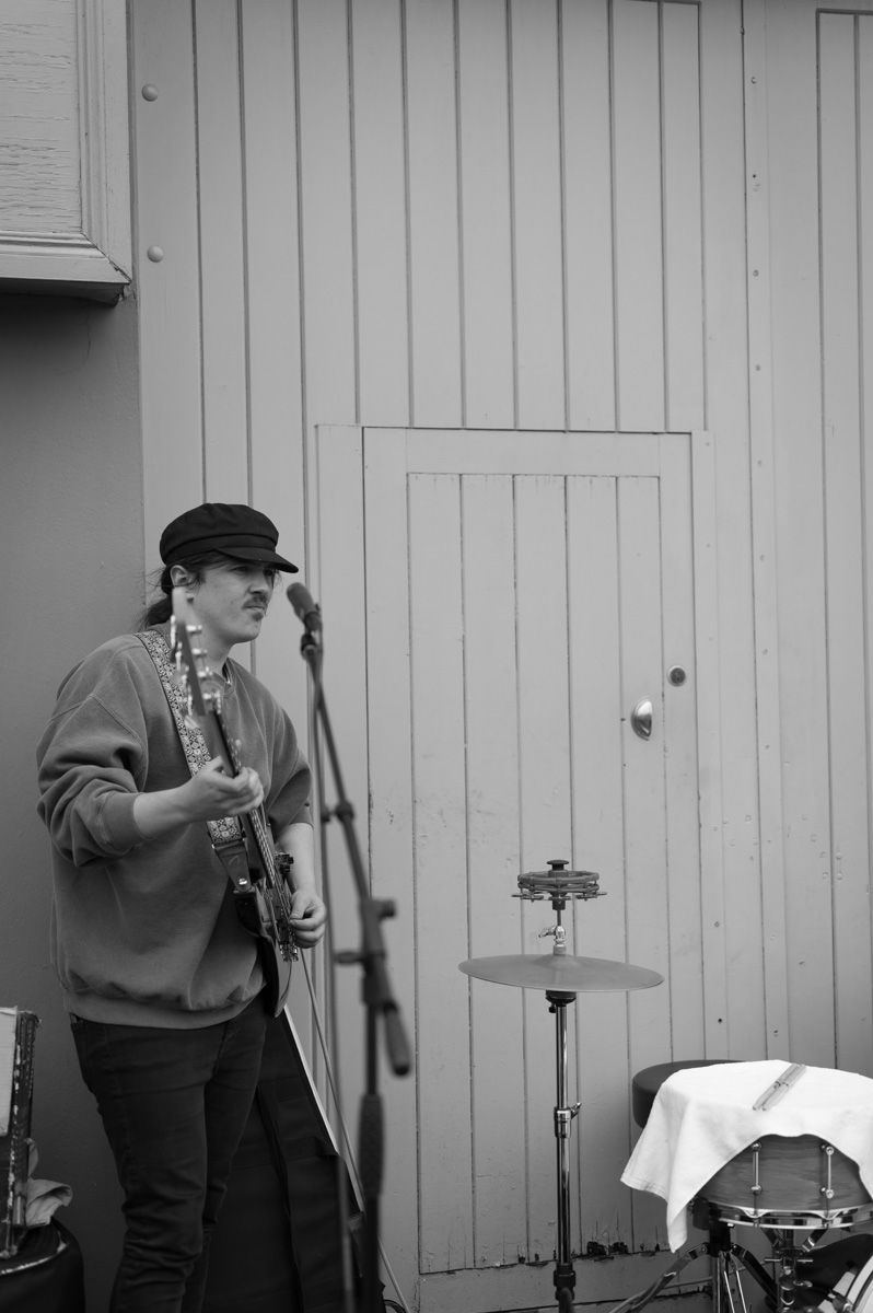 A busker playing guitar in front of a wooden fence.