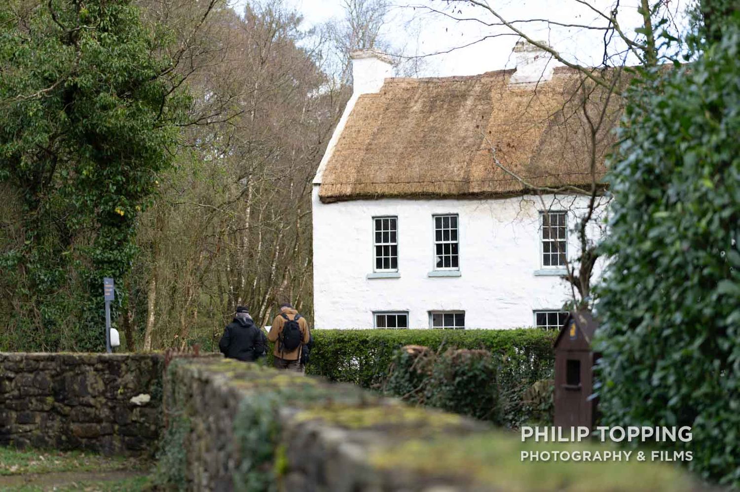 Two people walk past a white cottage.