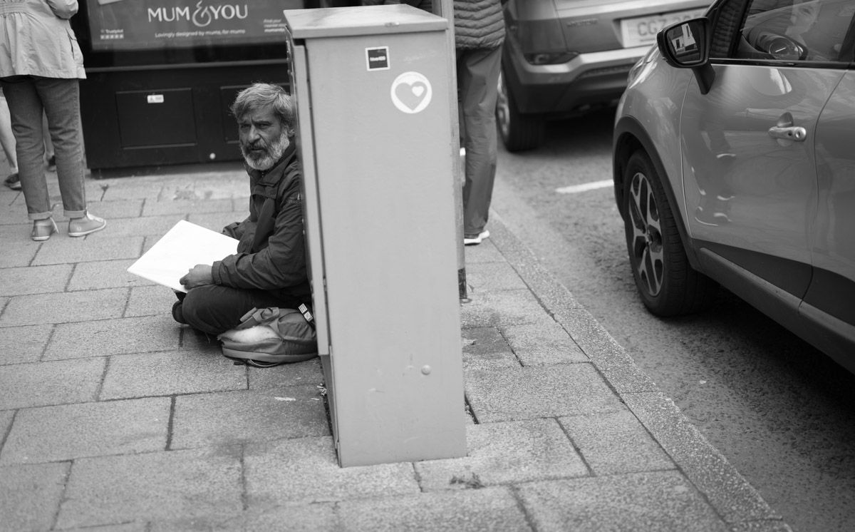 A tramp is sitting begging at the side of the street.