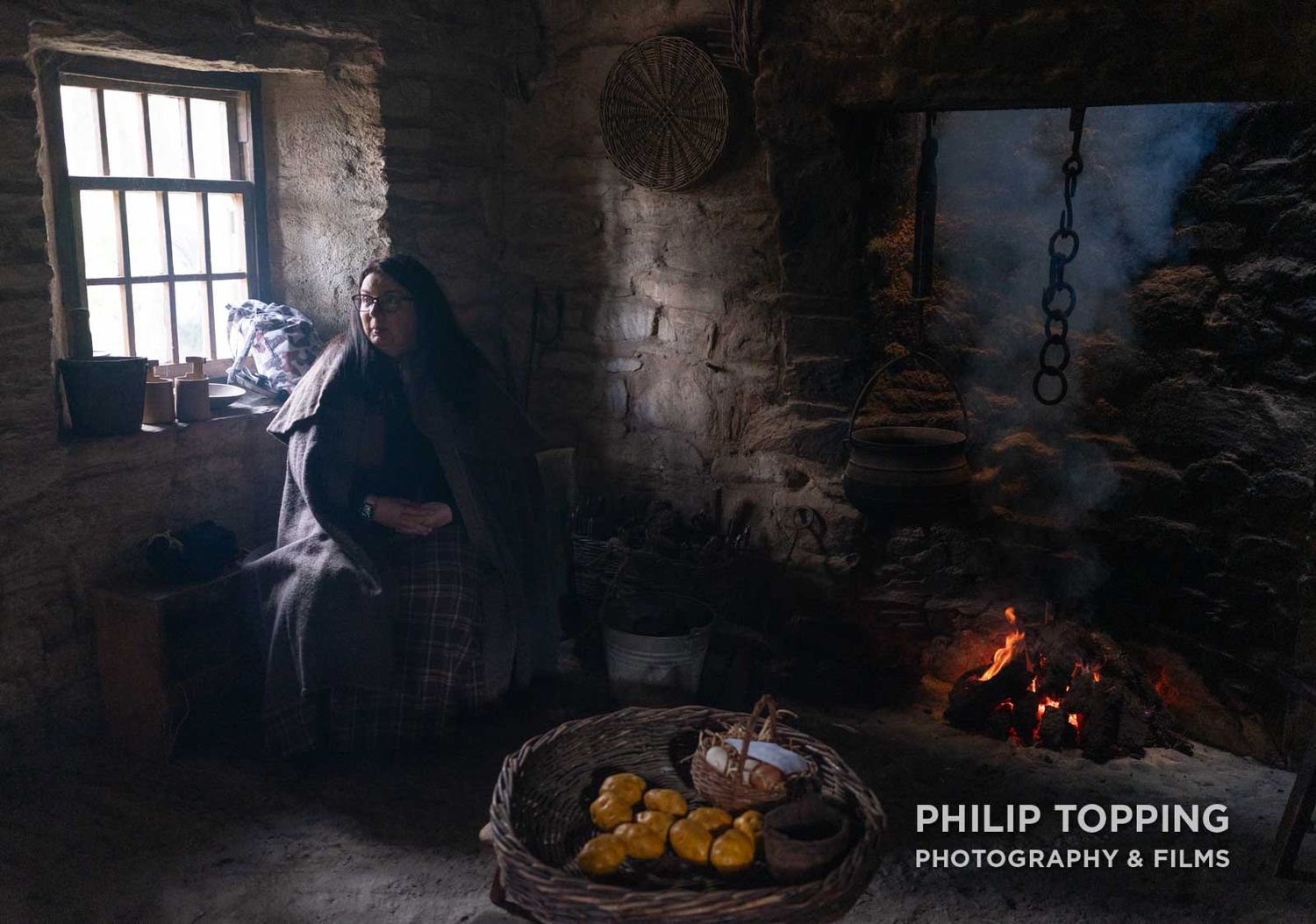 A woman dressed in Victorian clothes chats about life in old times beside the fire in the living room.