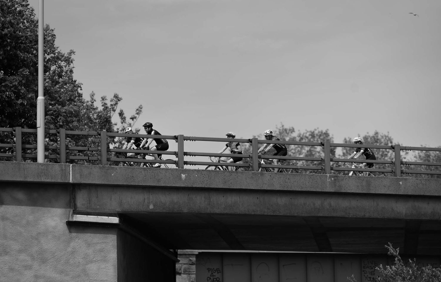 Cyclists cycling along the Northway are photographed from below.