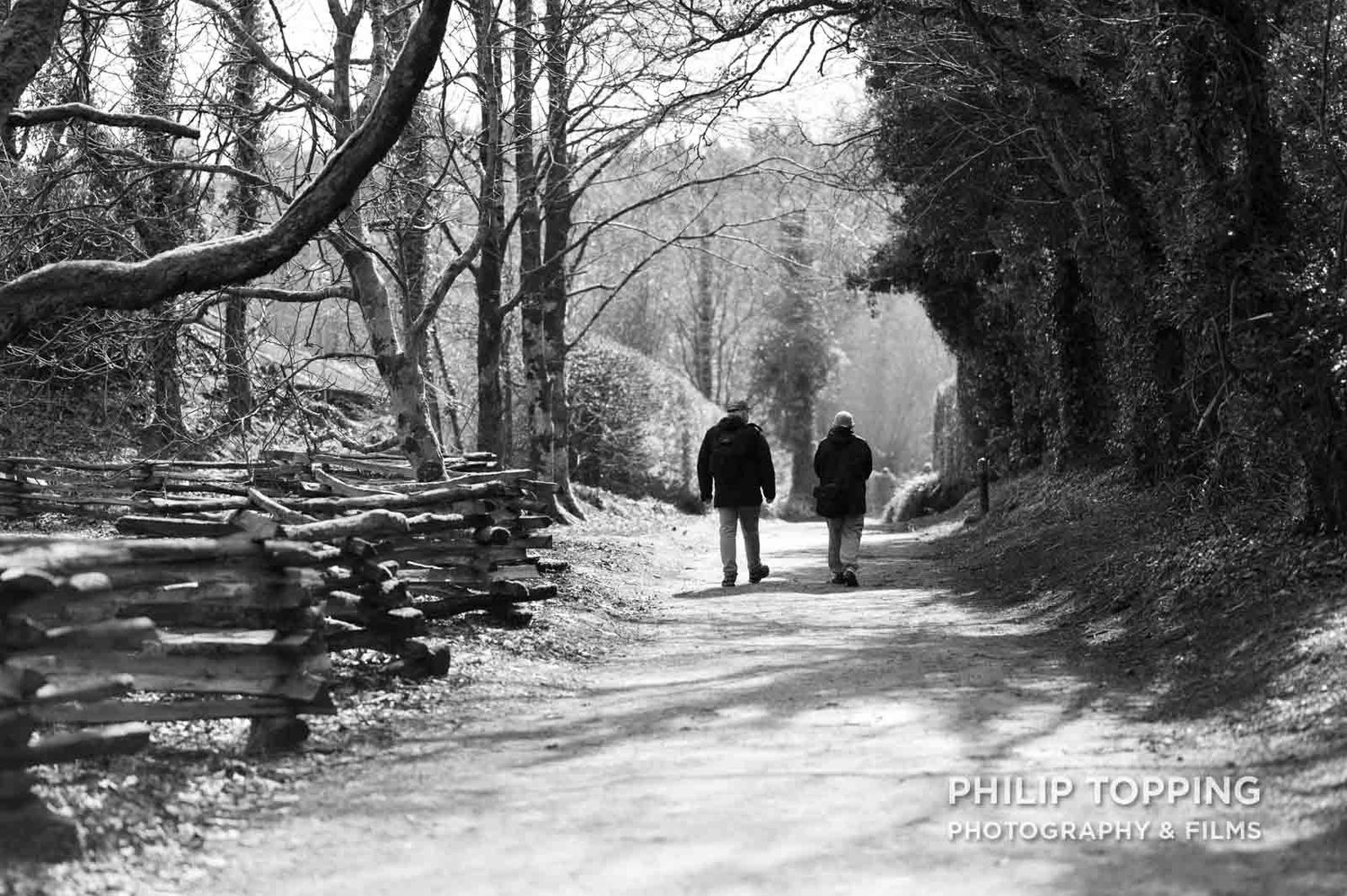 Two people walking along a path at Ulster American Folk Park in mono.