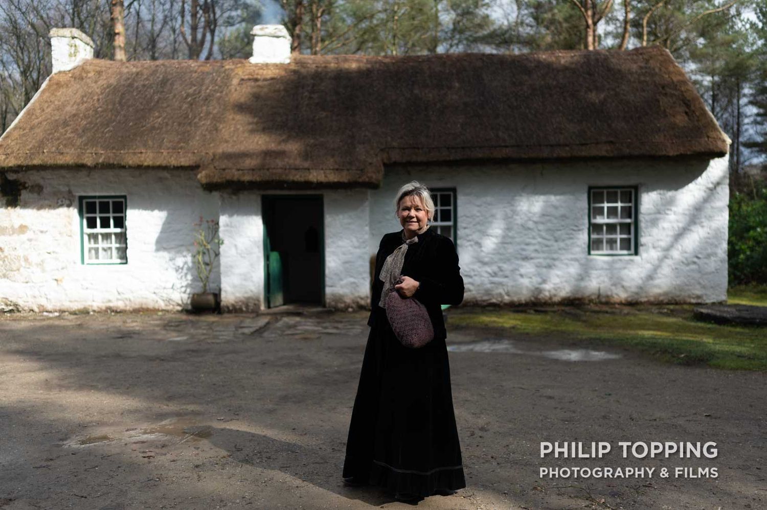 A female in costume is standing in front of the cottage.
