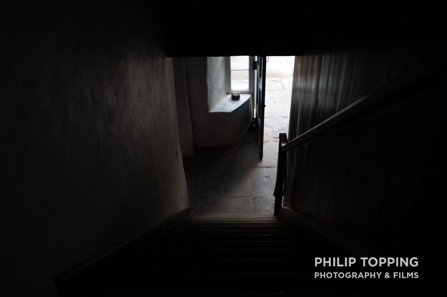 Dark, moody photo of a hallway with a door open, photographed from the stairs.