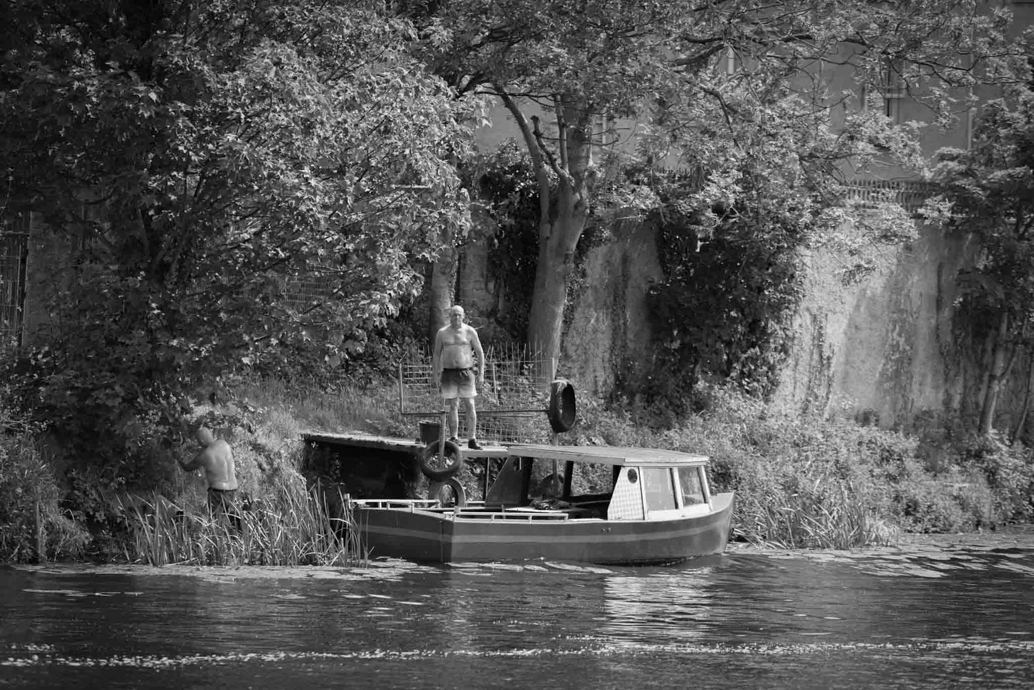 Two people are on a small boat at the side of the river.