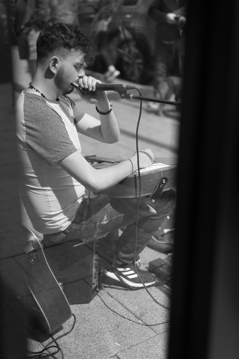 Close-up of a male playing a harmonica photographed through a window.