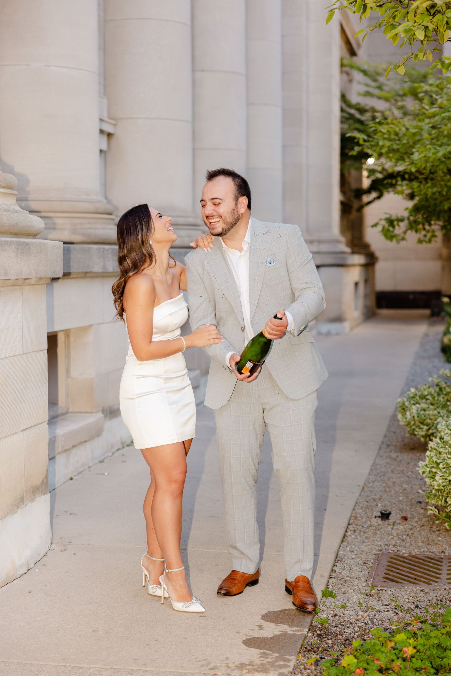 A well-dressed couple enjoys a champagne celebration beside classical architecture columns.