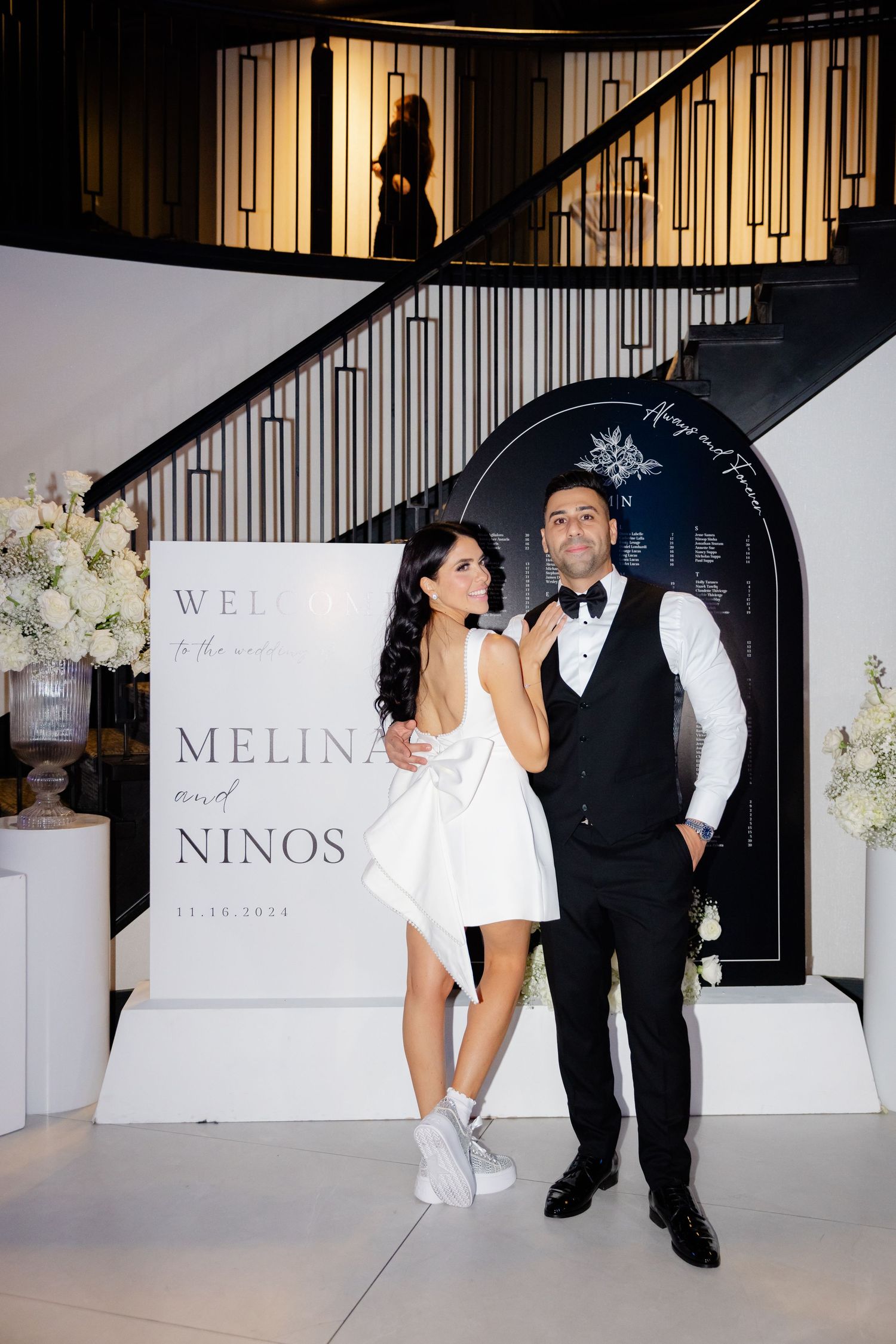 Bride in short dress and groom in vest pose together at wedding reception.