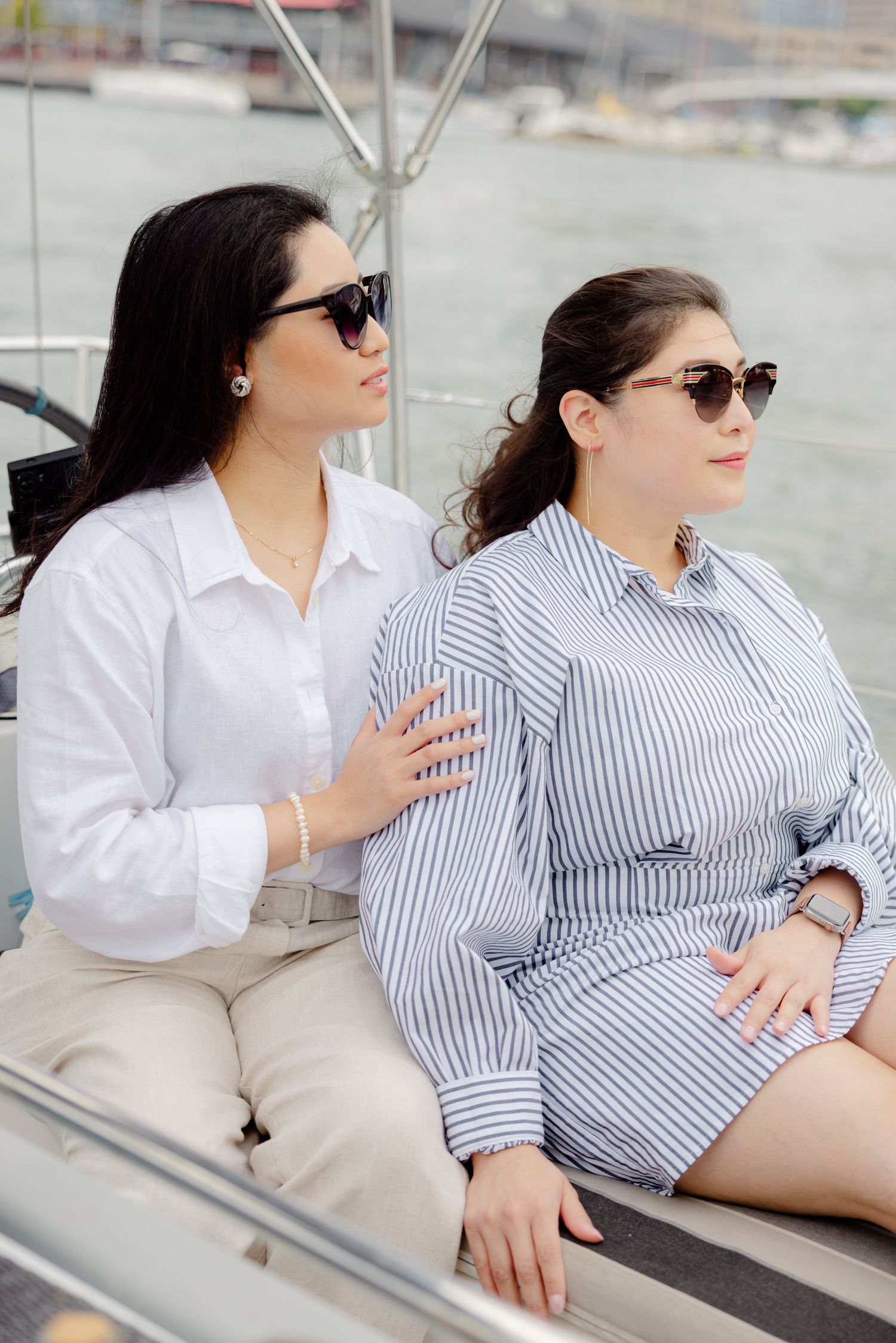 Two women in sunglasses relaxing on a boat deck, one wearing white and the other in a striped shirt.