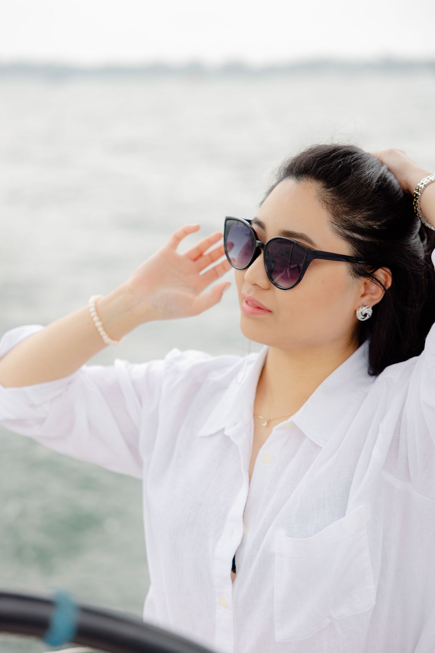 Woman in white shirt and sunglasses enjoying breeze on boat with water backdrop.